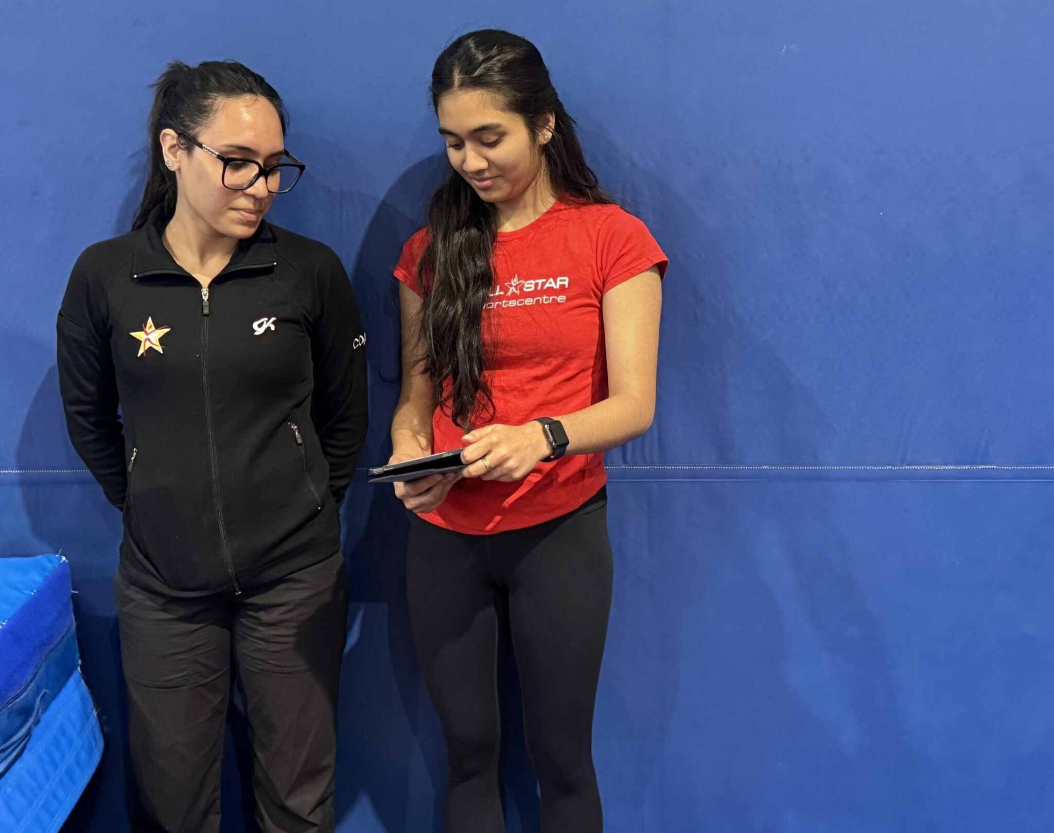 Teen coach-in-training assisting gymnastics instructor with young kids